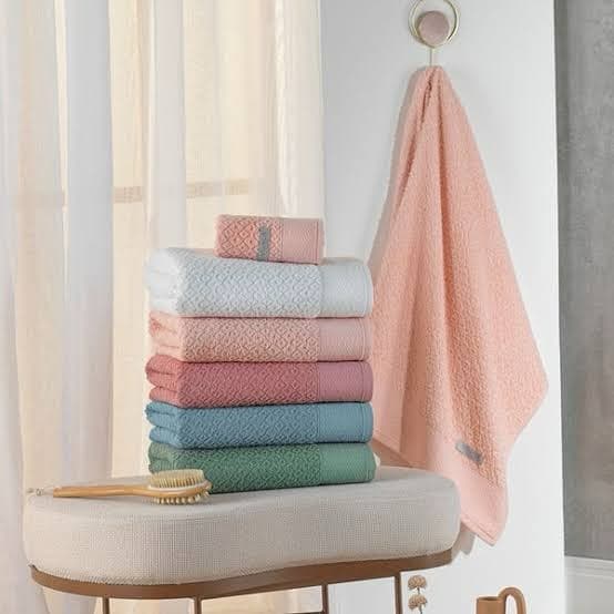 Toalhas de trama miúda empilhadas em branco, rosa, coral, azul e verde, com uma toalha pêssego pendurada ao lado