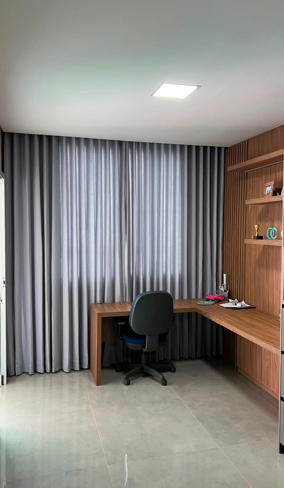 Home office com marcenaria de madeira e cortina blackout cinza cobrindo a parede da janela