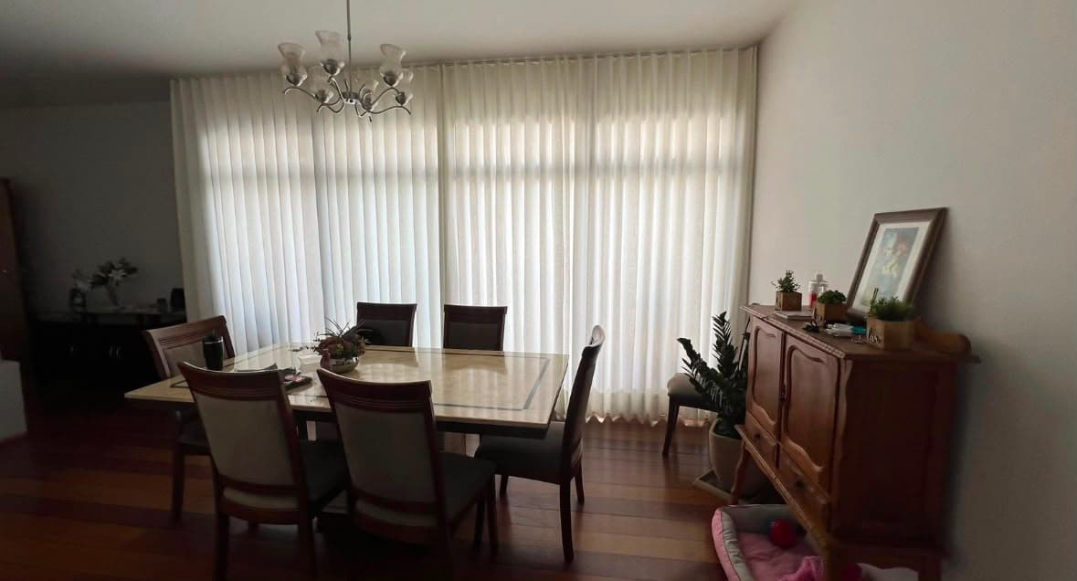Sala de jantar com mesa de seis lugares e cortina de voil branco cobrindo a parede envidraçada