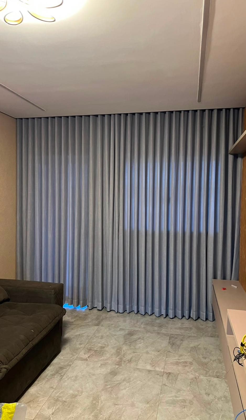 Sala de estar com sofá escuro e cortina cinza wave cobrindo toda a parede