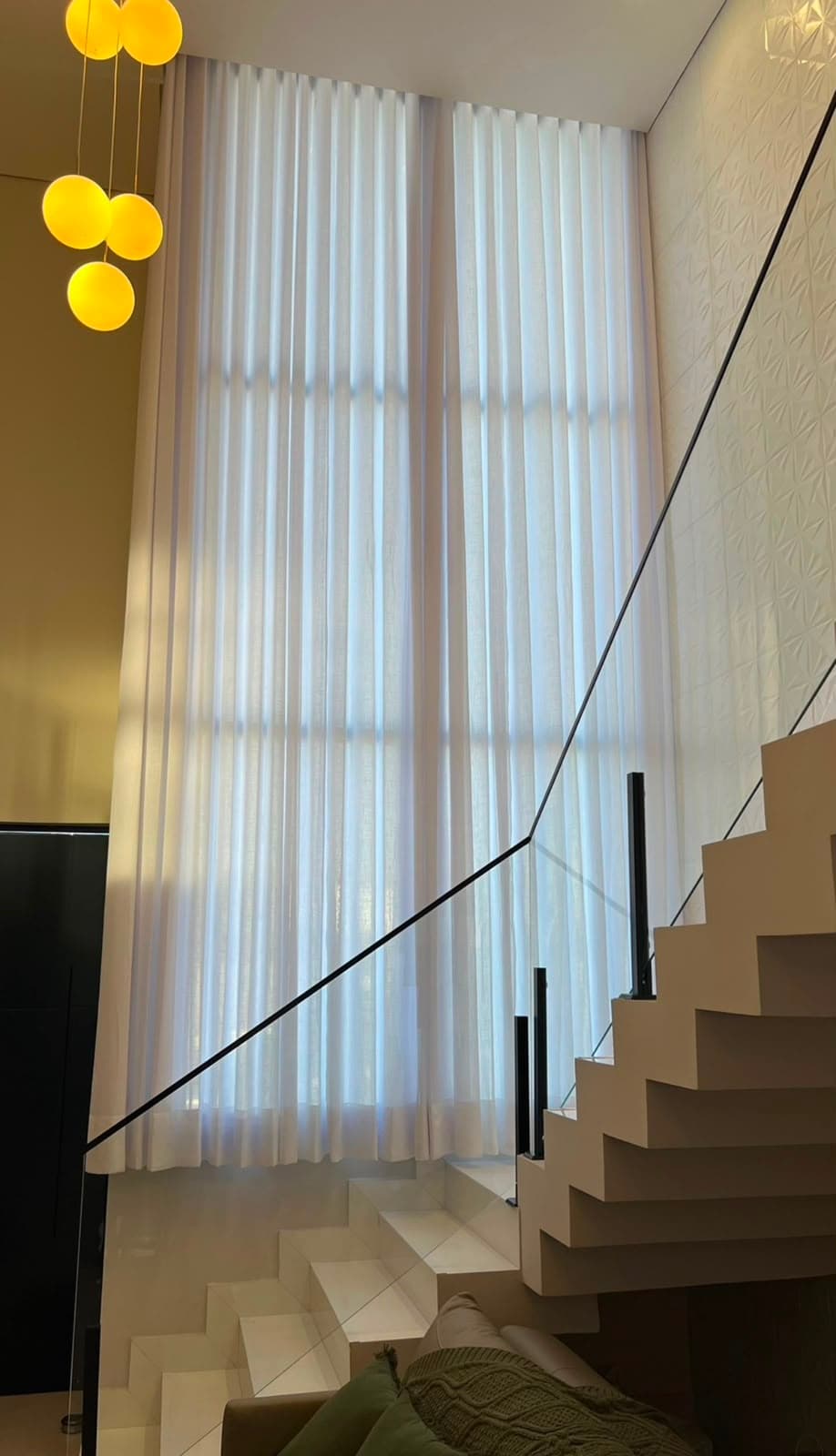 Vão de escada com cortina de voil branco de pé-direito duplo ao lado do guarda-corpo de vidro