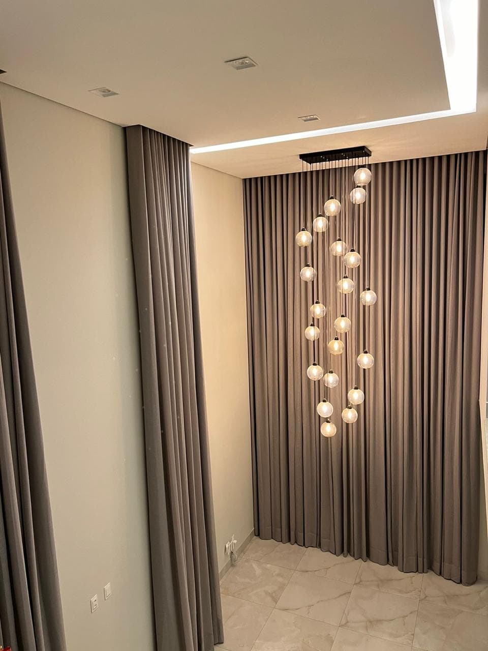 Hall com pé-direito duplo, cortina marrom-acinzentada do teto ao chão e lustre de esferas de vidro em cascata