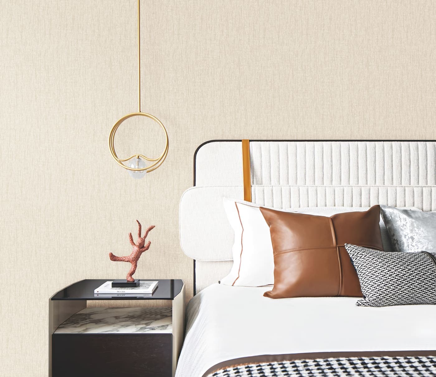 Quarto com parede revestida de papel de parede bege texturizado, cama branca com almofadas caramelo e pendente dourado
